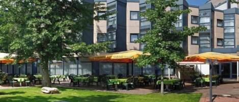 An outdoor area with tables and chairs, a small water feature, and a building with multiple floors and windows.