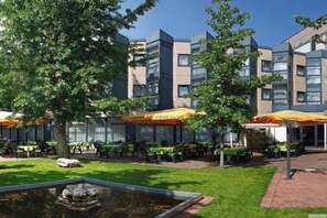 An outdoor area with tables and chairs, a small water feature, and a building with multiple floors and windows. - Sunday Hotel Köln Brühl (Bruehl)