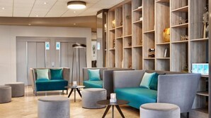 A modern lobby with a grey sofa, teal cushions, and a wooden bookshelf.