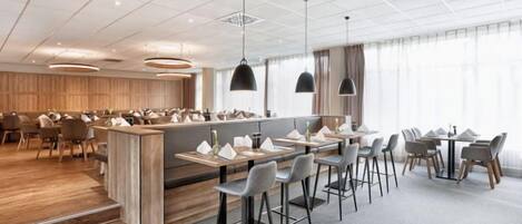 A modern hotel restaurant with a central bar, multiple dining tables, and a spacious layout.