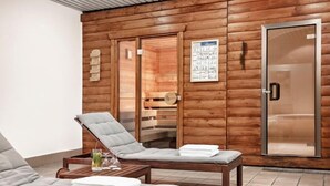 A spa room with wooden walls, two lounge chairs, a wooden table with towels, and a glass-enclosed shower area.