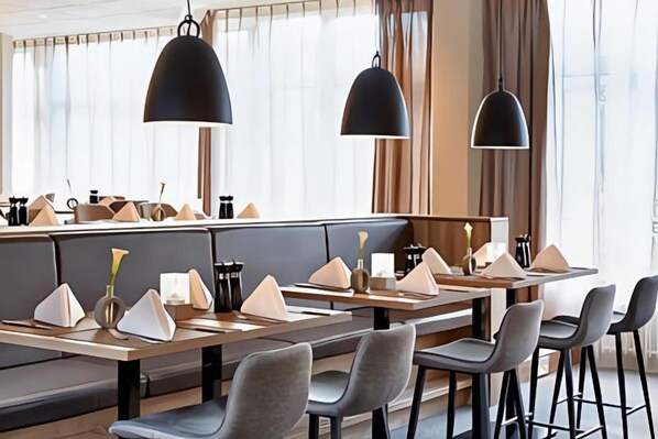 Un restaurante moderno con mesas altas, asientos acolchados, iluminación colgante y vistas amplias a través de grandes ventanales.