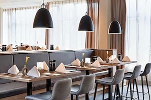 Un restaurante moderno con mesas altas, asientos acolchados, iluminación colgante y vistas amplias a través de grandes ventanales.