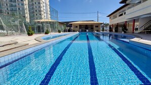 A swimming pool with clear blue water, surrounded by buildings and a fenced area. - COJMG0101 - Cond. Canto Belo Aeroporto (Salvador)