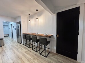 Modern kitchen with central island, pendant lights, stainless steel appliances, and a black door.