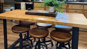Una cocina con armarios de madera, una isla central con taburetes, un rincón para café y una lámpara colgante.
