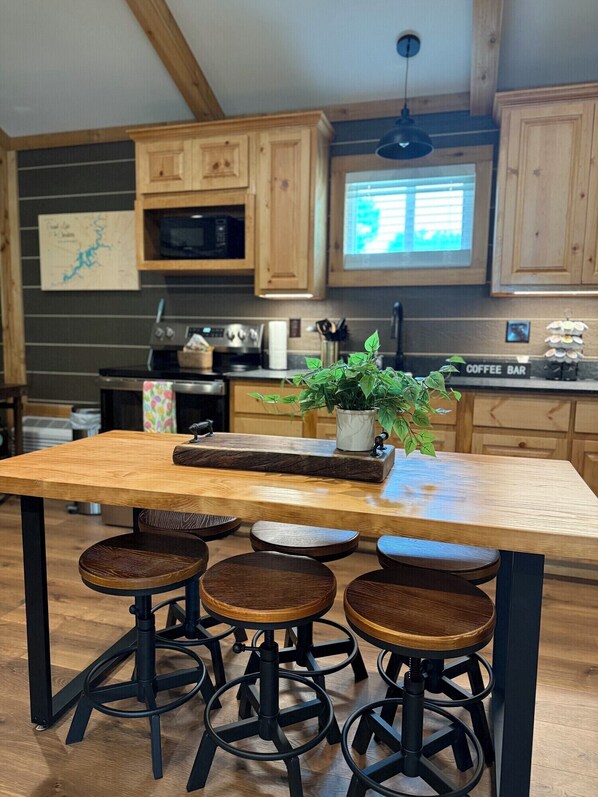 A kitchen with wooden cabinets, a central island with stools, a coffee bar, and a hanging light fixture.