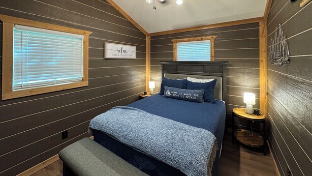 Un dormitorio con una cama, dos mesitas de noche, un ventilador de techo y una ventana con persianas.