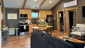 A modern kitchen with wooden cabinets, a dining area with a wooden table and chairs, a ceiling fan, and a sign that reads "Grand Lake Cabins".