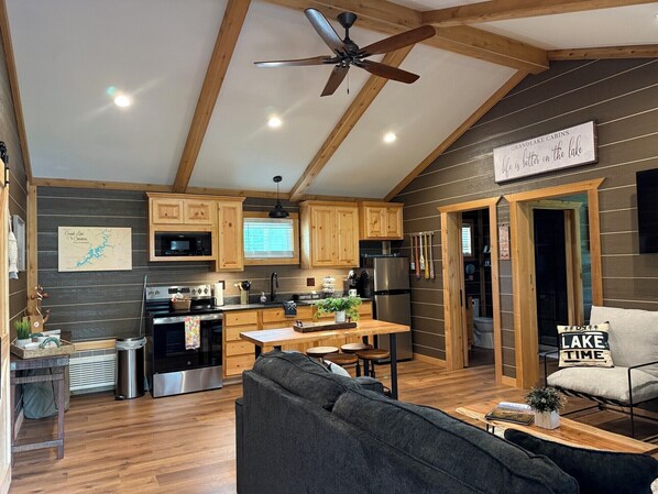 Una cocina moderna con armarios de madera, una zona de comedor con una mesa y sillas de madera, un ventilador de techo y un letrero que dice "Grand Lake Cabins".