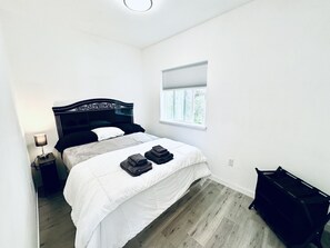 Een slaapkamer met een bed, nachtkastje, raam en een zwart meubel.