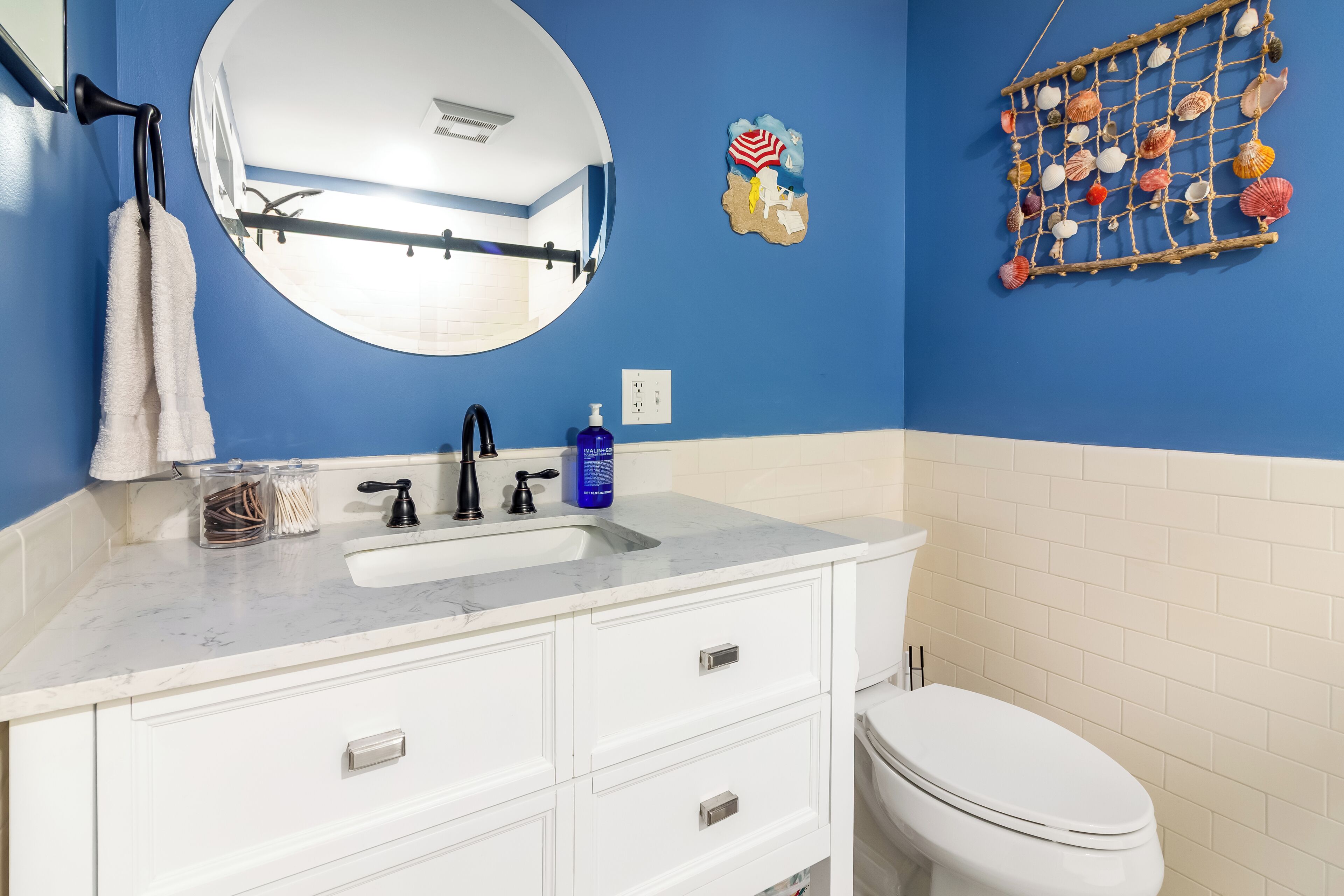 A bathroom with a blue wall, white vanity, and a white toilet.