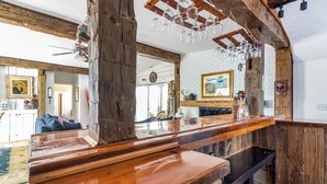 Un coin bar rustique en bois, doté d’un comptoir poli, de poutres apparentes et de verres à vin suspendus.