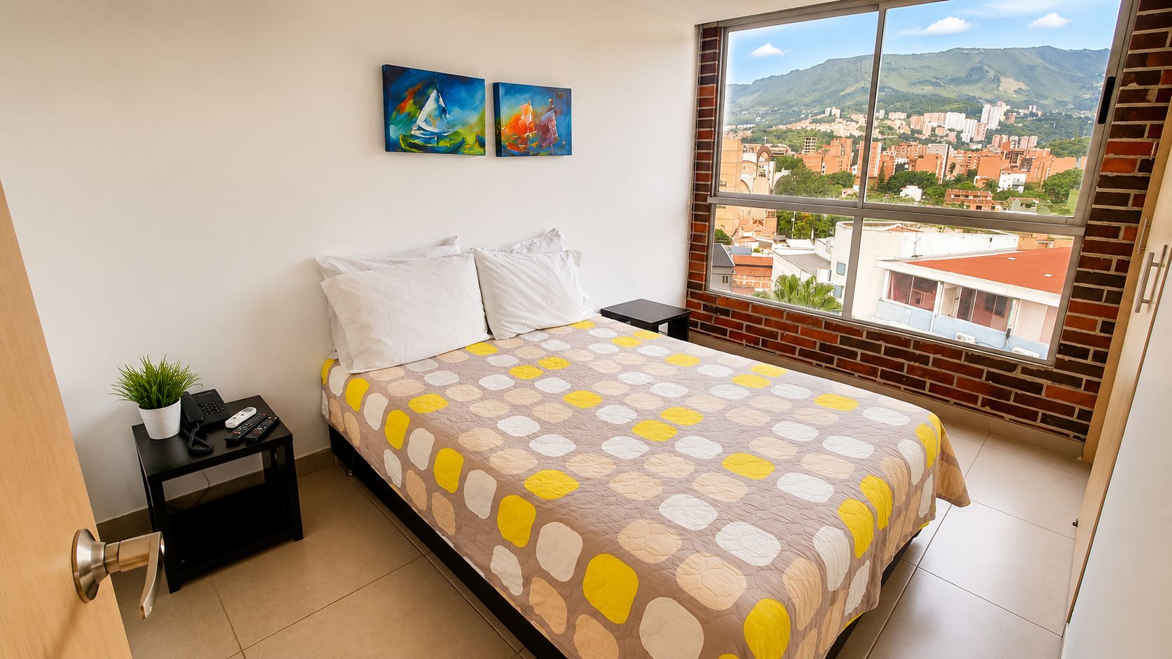 Une chambre à coucher avec un lit, une table de chevet, une plante en pot et une vue sur le paysage urbain par la fenêtre.
