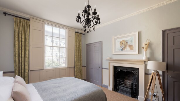 A bedroom with a bed, a chandelier, a fireplace, and a window with curtains.