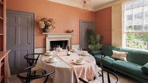 A dining area with a round table set for six, a green sofa, and a fireplace.