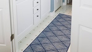 A bathroom with a granite countertop, white cabinets, a mirror, and a blue patterned rug.