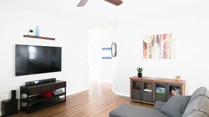 A modern living room with a flat-screen TV, wooden entertainment unit, grey sofa, and a small table with a plant.