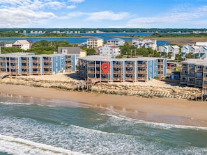 Un hotel frente al mar con edificios de varios pisos, una playa de arena y vistas al océano y la costa distante.