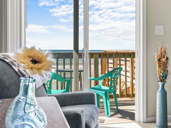 Un balcón con vista a la playa, un sofá, una silla y un jarrón con plantas secas.