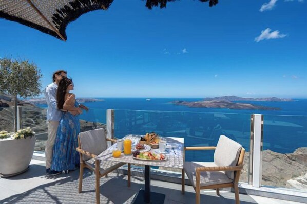 A couple standing by a table with a meal and a view of the sea.