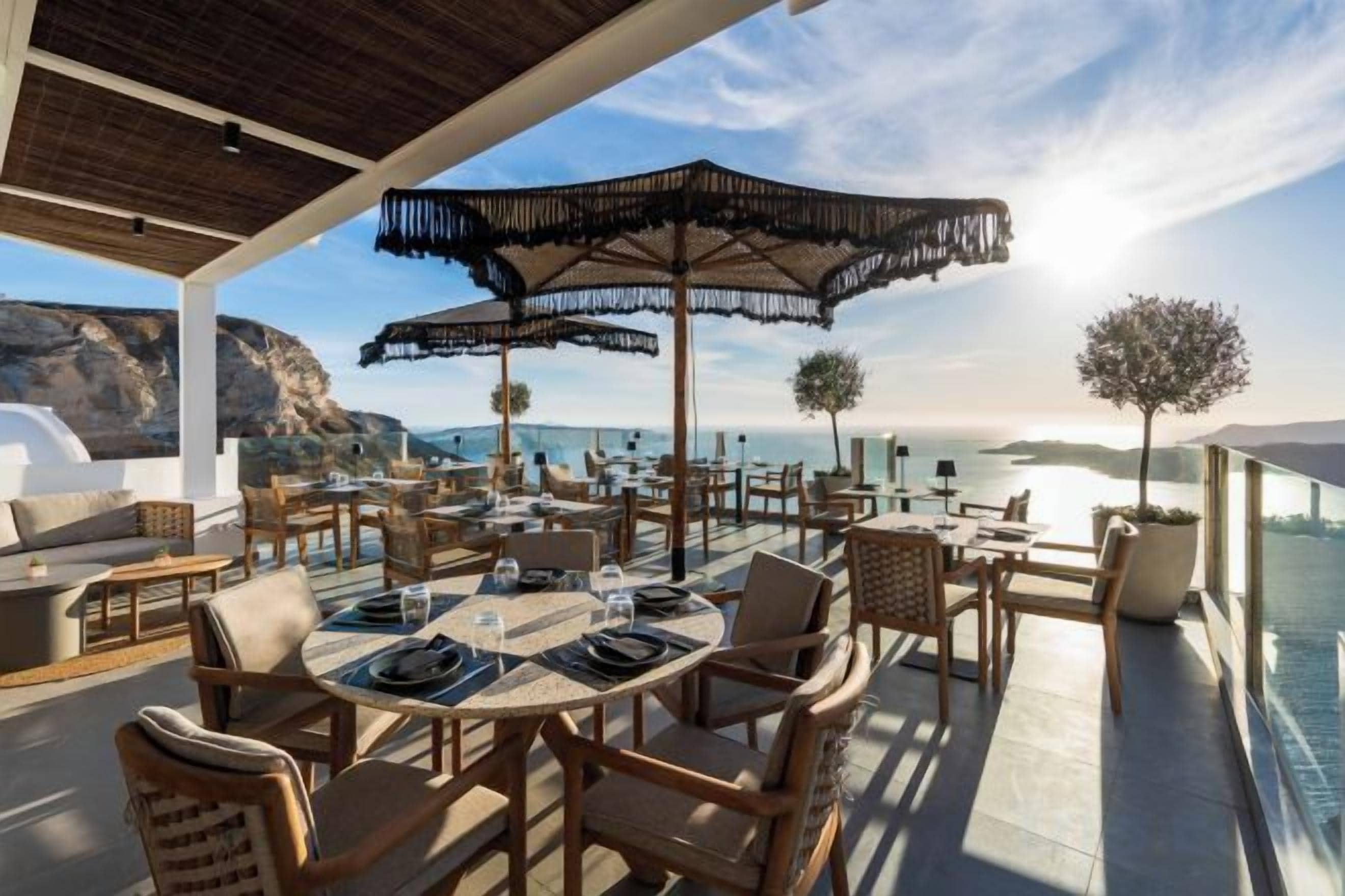 An outdoor dining area with tables and chairs, a large umbrella, and a view of the ocean.