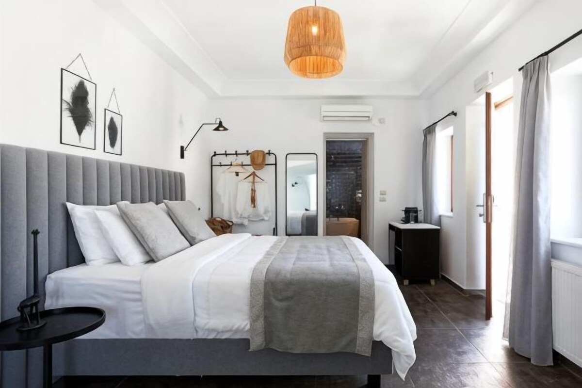 A bedroom with a bed, bedside tables, a hanging light fixture, and a view of the outdoors.