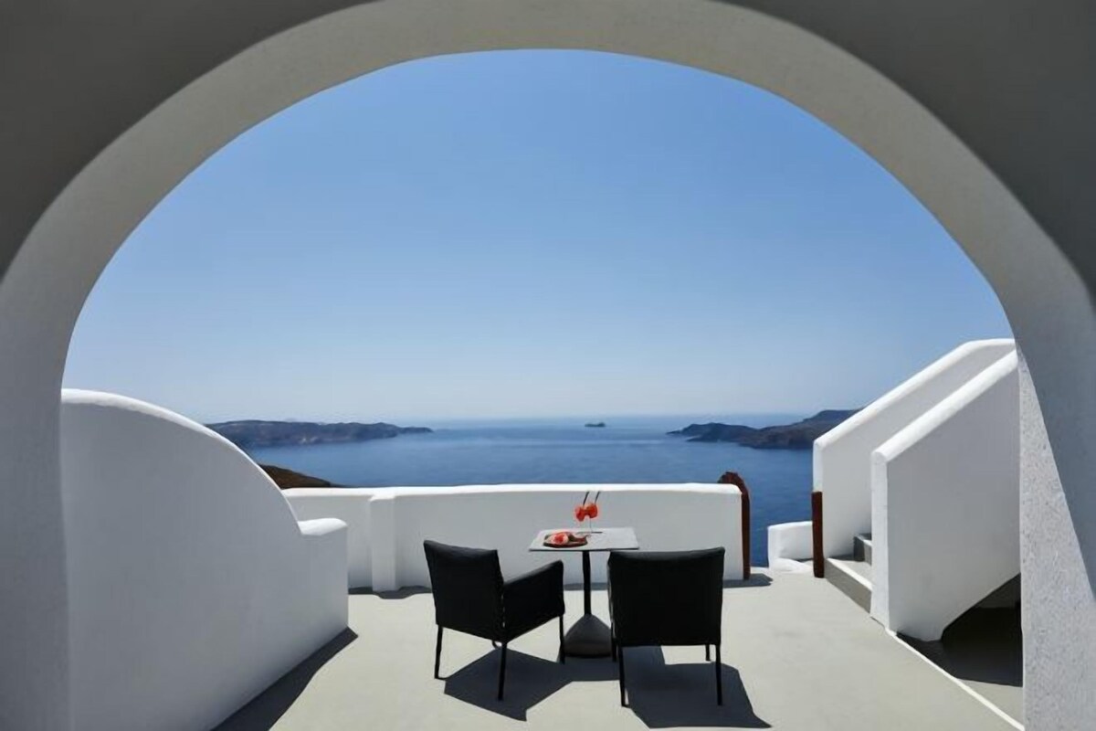 A dining area with a table and chairs, a view of the sea, and a white architectural structure.
