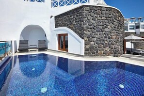 A swimming pool with a stone wall and white building.
