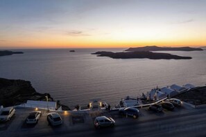 A coastal road with parked cars and a view of the sea at sunset. - Petit Palace Suites (Santorini)