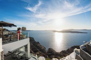 A coastal property with a terrace overlooking the sea, a glass balustrade, and a clear sky. - Petit Palace Suites (Santorini)