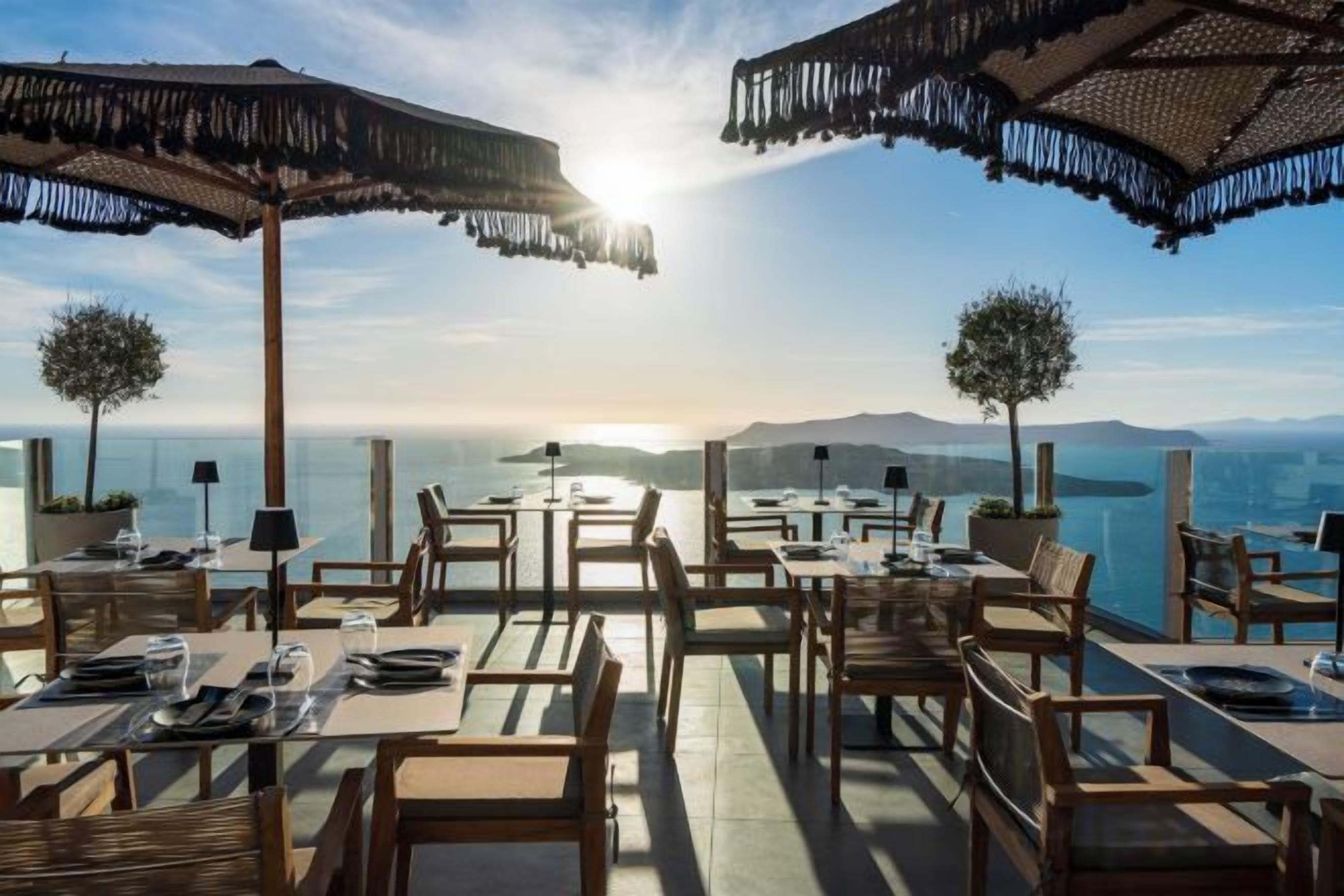 Un espace extérieur aménagé pour les repas, avec des tables, des chaises, des parasols et une vue sur la mer.