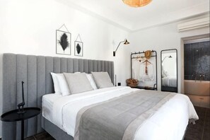 A modern bedroom with a large bed, a bedside table, a hanging light, and a mirror.