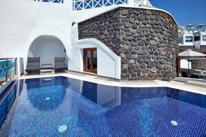 A swimming pool with a stone wall, lounge chairs, and a clear blue sky.