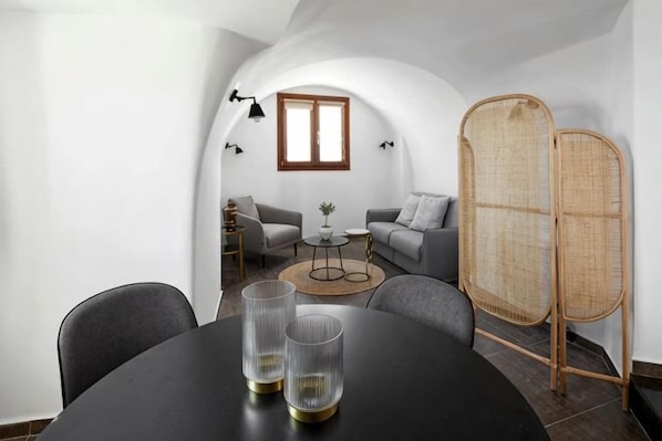 A dining area with a round table, two chairs, and two glass candle holders. - Petit Palace Suites (Santorini)