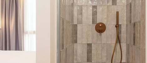 A modern bathroom with a shower, tiled walls, and a bed in the adjacent room.