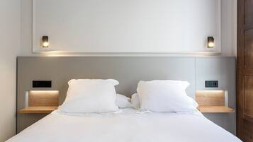 Un llit ben arropat amb llençols blancs, dues taules de nit amb il·luminació integrada i una paret sense decoració a la part superior.