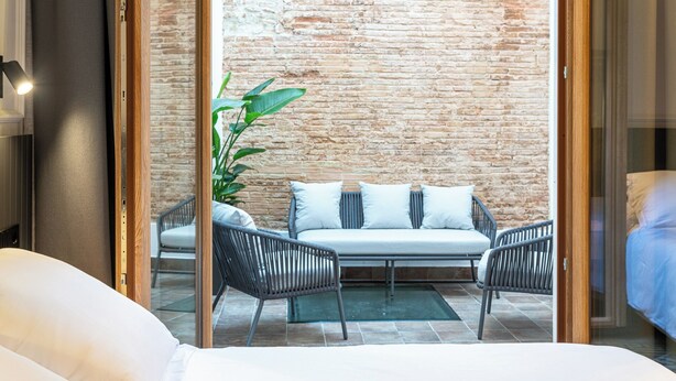 Une chambre d’hôtel avec un lit, un canapé, deux fauteuils, une plante en pot et un mur en briques.