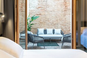 Habitación de hotel con cama, sofá, dos sillones, planta en maceta y pared de ladrillo.