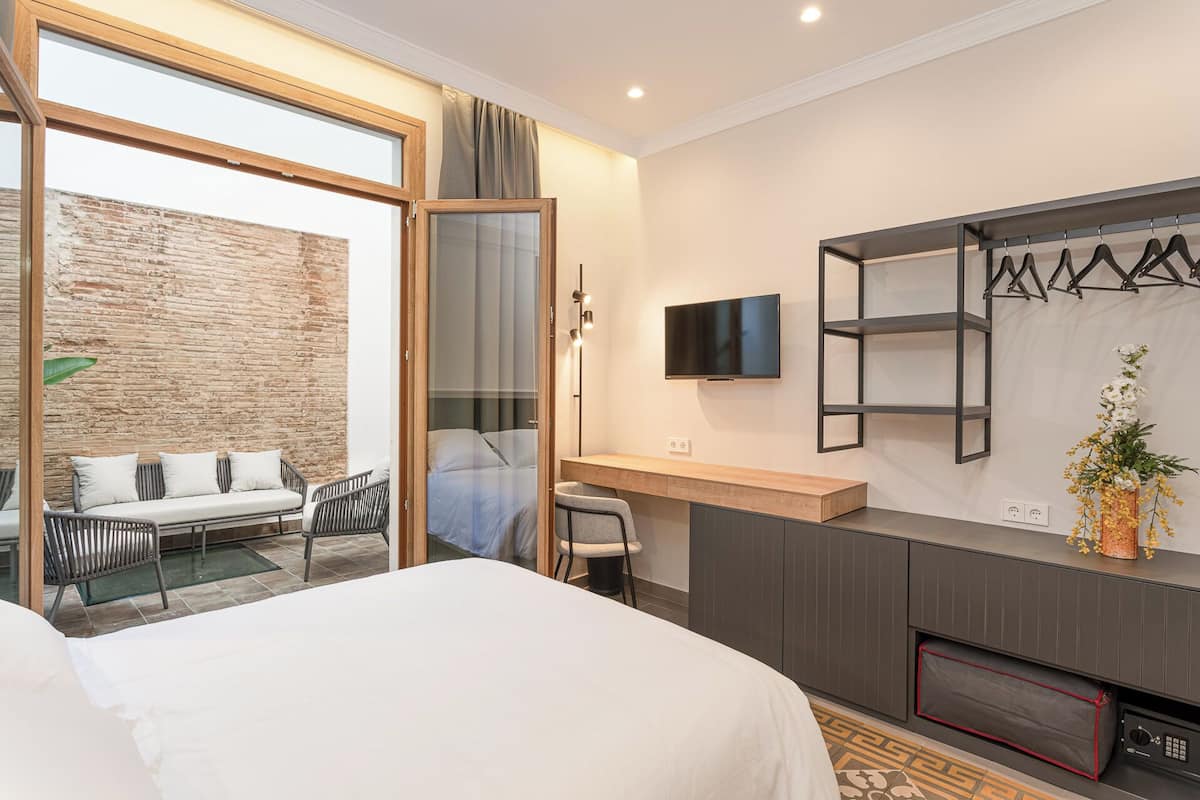 A modern hotel room with a large bed, a desk with a chair, a TV mounted on the wall, and a small seating area with a sofa and chairs.