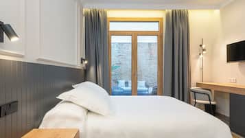 A hotel room with a bed, a desk, a chair, a TV, and a window with curtains.