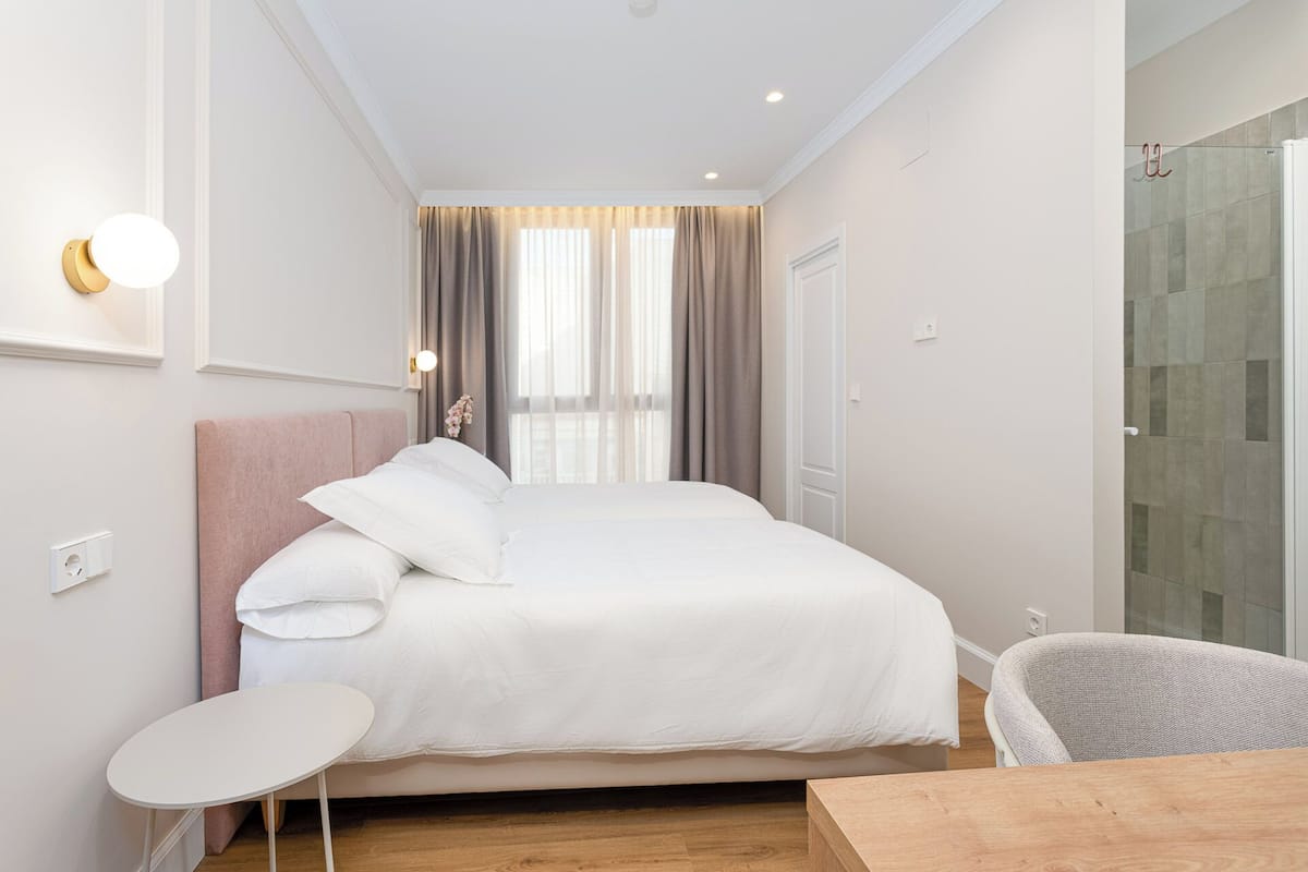A hotel room with a bed, a small table, a chair, and a shower area.
