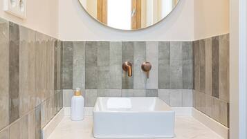 Un baño con un espejo ovalado grande, un lavamanos rectangular y un perchero para toallas.