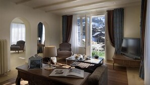 Un soggiorno con televisore, un tavolo con libri, una poltrona e vista su un paesaggio innevato attraverso ampie finestre.