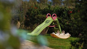 Een kinderspeeltuin met een glijbaan en schommels in een tuin.