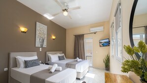 Een hotelkamer met twee bedden, een plafondventilator, airconditioning aan de muur, een televisie en een houten tafel.