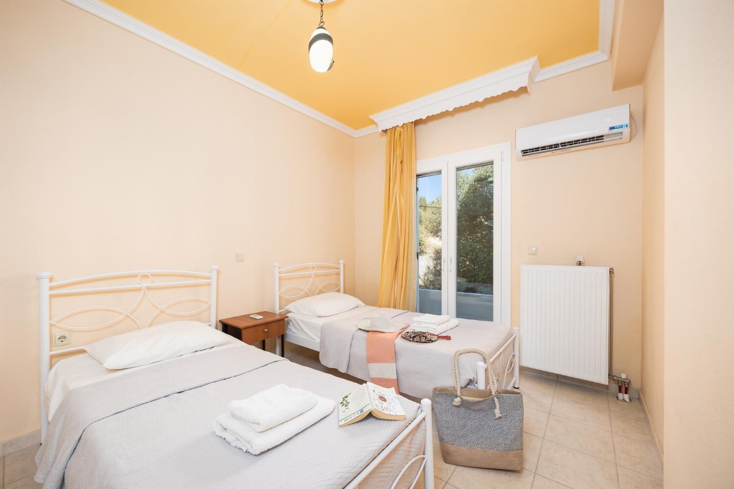 A bedroom with two beds, a window with curtains, an air conditioning unit, and a radiator.
