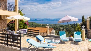Una terraza con sillones de sol, sombrillas y una vista panorámica del mar.