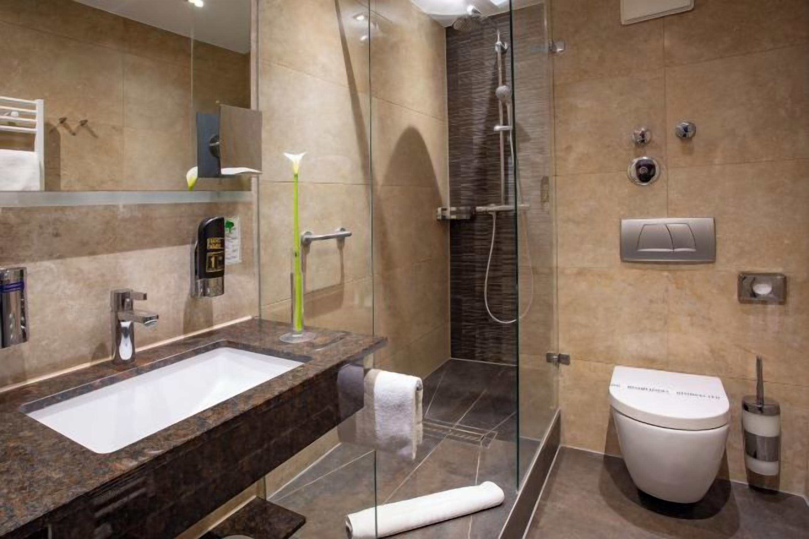 A modern bathroom with a marble sink, a glass shower enclosure, a toilet, and a towel.