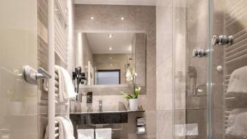 A modern bathroom with a glass shower enclosure, a marble-tiled wall, a large mirror, and a potted orchid.